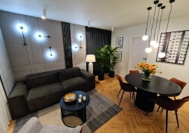 Ważne miejsca w pomieszczeniu podświetlają różnego rodzaju lampy. „Kamienną” ścianę zdobią czarne kinkiety od Nowodvorskiego. Przy kanapie stanęła biała lampa od 4concepts. Nad stołem wiszą kule marki Kaspa, a przy telewizorze lampy-tuby z Ramko.