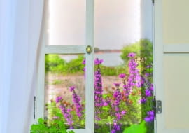 Trudno oprzeć się wrażeniu, że przez to okno rozpościera się widok na łąkę i jezioro. Na pierwszym planie kwitnące wrzośce.