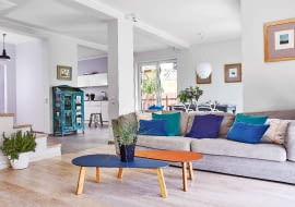 PRZESTRZEŃ I ŚWIATŁO - w tym domu z pewnością ich nie brakuje. Kąt wypoczynkowy od kuchni i jadalni wizualnie oddziela podłoga: w salonie położono bielony dąb szczotkowany, w pozostałej części gres. Szarą kanapę, stoliki kawowe Melisa w odcieniach dżinsu i brandy, zielone i granatowe poduszki oraz osłonki na do- niczki z trawą i rozmarynem kupiono w sklepie Nap.