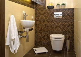 Układ idealny. Brązy, beże i dekoracyjne płytki z motywem liści, które podkreślają kształt wnęki nad podwieszanym sedesem.