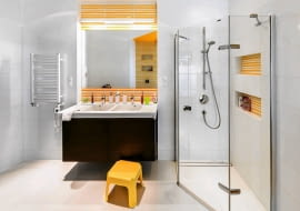 ŁAZIENKA. W kabinie prysznicowej nie ma brodzika (tylko odpływ liniowy w podłodze), dzieci mogą więc bezpiecznie do niej wchodzić i wychodzić. Dolna wnęka-półka znajduje się na takiej wysokości, że Amelka i Brian bez trudu sięgają po kosmetyki. Łazienka jest jasna, zaaranżowana w biało-żółtej kolorystyce. Zdaniem projektanta to uniwersalne zestawienie barw, które szybko się nie znudzi (nawet gdy dzieci podrosną).