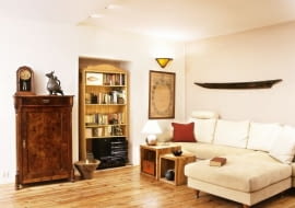 W kąciku wypoczynkowym wokół nowoczesnej kremowej kanapy można dostrzec wiele oryginalnych przedmiotów: pachnącą cygarami kubańską szafeczkę, metalowy egipski gong.