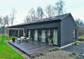 DOM ma nietypowy kształt i równie niebanalny kolor - otynkowano go na grafitowy odcień. Od wiosny do późnej jesieni życie rodzinne i towarzyskie przenosi się na taras z modrzewiowych desek.