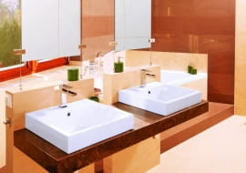 Łazienka 1. Wannę na podeście przesłaniają dwie ścianki podtrzymujące blat z umywalkami oraz lustra, które zamocowano na stalowych linkach rozpiętych pomiędzy ściankami a sufitem. W strefie kąpielowej przeważają brązowe płytki, w pozostałych - beżowe.