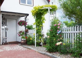 Przy domu w sezonie bujnie rosną kwiaty. Obrośnięta pnączami pergola to wejście do przydomowego ogródka.