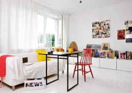 Wszechobecna biel powiększa optycznie małe mieszkanie (38 m kw.). Blaty szafek (takie same wiszą w kuchni) pełnią funkcję biblioteczki i miejsca na bibeloty i zdjęcia. Na podłodze - malowane deski. Kotka Sissy, trzeci domownik, puszy się na oparciu kanapy.