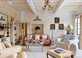 Stone floored provencal sitting room with armchairs, floral sofa throw and distressed wooden coffee table SLOWA KLUCZOWE: provence france french provencal inside indoors day nobody interior design home living room drawing room sitting room sofa floral pattern cream colour artwork seating area animal likeness swan bird shelves shelving tiled floor painted furniture shabby chic white white colour armchair country style horizontal image colour image