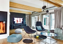 Za ścianą z telewizorem (wykończonej tapetą marki Elitis) znajduje się biblioteka i mały gabinet. Centralnie zainstalowany kominek zapewnia możliwość taniego ogrzania całego domu. Podłogę na parterze i piętrze pokrywa bielony dąb olejowany (Parkett Service).