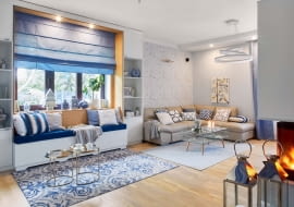 W salonie zwracają uwagę dodatki - chińskie wazy, poduchy w paski i marokańską koniczynkę, wzorzysty dywan (z Mint Grey i Raw Decor). Do tapety z motywem kwitnących gałązek wiśni idealnie pasuje obraz Ivy Białopiotrowicz, na którym rozsiadło się żółte ptasie stadko. Kominek, poprzednio zainstalowany pośrodku salonu, został zamieniony na model narożny, tak by był widoczny zarówno z salonu, jak i jadalni. Światło i wzór: spójrzmy czasem w górę. Ciekawa lampa sufitowa potrafi naprawdę przykuć wzrok. Dla całej rodziny bardzo ważne jest wspólne spędzanie czasu. Stąd pomysł na dodatkowe wygodne siedzisko w salonie. Umieszczono je we wnęce - do jej zbudowania wystarczyły dwie wysokie szafki po bokach okna i rama z płyty gipsowo-kartonowej. Zainstalowano w niej oświetlenie. Złote stoliki kawowe są z Zara Home.