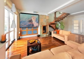 Gospodarze kochają podróże, co znalazło odzwierciedlenie w wystroju domu. Do ich wojaży po bliższych i dalszych zakątkach świata nawiązują nie tylko rozstawione po całym wnętrzu pamiątki, ale także egzotyczne gatunki drewna i... kolorystyka błękitnej jak ocean sypialni. <BR /> DOM. Ściana ciekawie zaaranżowana. Okno przesłonięte ekranem, na którym gospodarze oglądają filmy z projektora, to w rzeczywistości wbudowany w ścianę regał. Dwanaście frontów z  mlecznego szkła ujęto w ramę z palisandru. Tym samym materiałem obramowano palenisko kominka wyłożonego płytami wielobarwnego łupka. Na podłodze - orzech amerykański.