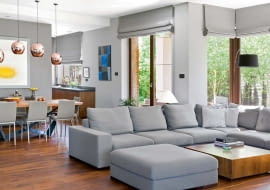 Odcienie szarości kontrastują z ciemną podłogą (orzech amerykański). Przy sofie stolik z tego samego drewna, co podłoga, wykonany przez pracownię stolarską Macieja Pióro. Pod oknem lampa Twiggy, Foscarini. Szaro-błękitny obraz autorstwa Zbigniewa Gręziaka.