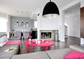 Wystrój domu miał być stonowany kolorystycznie, z przewagą naturalnych barw ziemi. I taki jest. wystarczyło kilka akcentów w ostrym różu, by wnętrza nie wyglądały monotonnie. <BR /> DOM. Ściana z kominkiem oddziela część kuchenno-jadalną od wypoczynkowej. We wnętrzu przeważa kolor szary. Takie są zarówno ściany (także ta z przecierkami, będąca obudową kominka), jak i zrobiona na zamówienie duża kanapa oraz krzesła przy kuchennym stole.