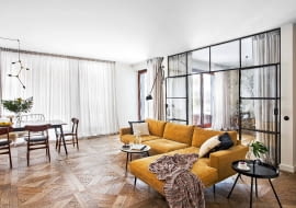 Strefę dzienną mieszkania wyodrębniono innym wzorem podłogi. Przy stole (BoConcept) komplet krzeseł vintage (Przetwory). Miodowa kanapa BoConcept, stolik kawowy Westwing.pl.