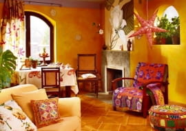 Radość płomiennych kolorów. Zastosowanie w salonie tak intensywnych barw wymaga wprawdzie pewnej odwagi, ale efekt wart jest ryzyka. Pod warunkiem oczywiście, że dobrze się czujemy w otoczeniu mocnych kolorów. A te są tutaj wszędzie - począwszy od ścian i podłogi, a skończywszy na tkaninach ozdobionych wyrazistymi kwiatowymi motywami. Taka feeria barw podniesie temperaturę w pomieszczeniu co najmniej o kilka stopni...