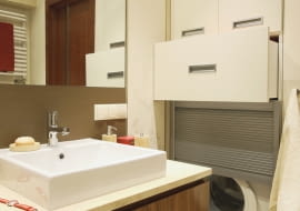 Pralkę przesłaniają drzwi z aluminiowych żaluzji. Nad nią we wnęce znajdują się szuflady i szafka z płyty MDF zamykana drzwiczkami.