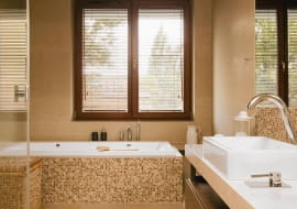 <B> Pojedynczy nie zdziała we wnętrzu wiele, ale w grupie zyskuje moc - ożywia kolorystykę, podkreśla kształt mebli i urządzeń, zdobi. W łazienkach nastał czas mozaiki. </B><BR /> WNĘTRZA: Gospodarze wykończyli mozaiką obudowę wanny oraz ścianę przy umywalce i w kabinie prysznicowej, a więc miejsca najbardziej narażone na kontakt z wodą (wybrano produkt z polerowanego marmuru Emperador włoskiej firmy Sicis). W ten sposób wizualnie podkreślono też strefy mycia i kąpieli. Oprócz mozaiki w łazience zastosowano gres imitujący polerowany trawertyn (płytki 30 x 90 cm i 60 x 90 cm układane na przemian). Odcienie kamienia idealnie pasują do kolorystyki całego wnętrza - na kostkach powtarzają się barwy pozostałych elementów wyposażenia (biel ceramiki, brąz mebli i dodatków, beż gresu). Ciepłe odcienie budują klimat sprzyjający odpoczynkowi. Lustro nad umywalką od góry i od dołu otaczają pasy mozaiki tworzące rodzaj ramy. Do wanny dobudowano schodek wykończony (tak jak cała podłoga) płytami gresu imitującego polerowany trawertyn. W podwieszonym suficie zainstalowano halogeny - dzięki temu można było zrezygnować ze światła sufitowego o dużej mocy i zawiesić jedynie ozdobną lampkę.