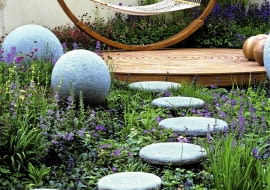 Modern outdoor room has unifying theme of circles and spheres.Concrete balls and stones lead to deck and hammock. Blue ajuga, nepeta and geranium SLOWA KLUCZOWE: Designer Garten Hof Holz H ngematte Kreis Kreise Pflanze Stein Storchschnabel Storchschn bel Trittsteine Wege ausspannen bl´hend enspannen entspannend entspannt erholend friedlich friedvoll geschwungen kreisf^rmig krumm modern relaxed relaxen ruhen zeitgen^ssisch Nicola Stocken Tomkins quadratisch