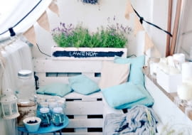 Jest tu wszystko, co potrzebne do relaksu: ława wymoszczona poduchami, stolik do odstawiania napojów, zasłonka (będąca też moskitierą), oświetlenie... A pod ścianą kwietnik z palety - lokum dla lawendy.