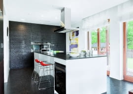 W tym domu rodzina i znajomi najchętniej zbierają się wokół dwóch mebli - stołu w jadalni oraz wyspy, zajmującej w kuchni centralne miejsce. Jest ona na tyle duża (323 x 123 cm), że może przy niej wspólnie gotować kilka osób, nie przeszkadzając sobie nawzajem; mniej zaangażowani w pracę będą w tym czasie"kibicować", siedząc na stołkach barowych. Całą kuchnię zaaranżowano w czerni i bieli; blat wyspy i podłoga są z granitu, fronty wysokiej zabudowy - z płyty MDF fornirowanej szczotkowanym i bejcowanym dębem.