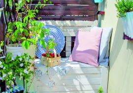 Oparcie balkonowej ławy zostało namalowane na drewnianym ekranie. Na pierwszym planie pomalowany na niebiesko wiekowy kociołek w roli donicy.