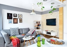 STONOWANE BARWY. W całym mieszkaniu dominują spokojne beże, biele i szarości, żywsze kolory występują tylko w dodatkach. W ścianie, na której wisi dziś telewizor, była niepraktyczna wnęka. Architektka zlikwidowała ją (powiększając dzięki temu garderobę), a nowo postawioną ścianę wyłożyła płytkami imitującymi cegłę (sklep Bartico). Pod sufitem zaprojektowała ramę z płyty gipsowo-kartonowej, w której zamontowano oświetlenie punktowe. Kanapa jest ze sklepu Agata, dywanik z decoretro.com.pl Obrazy na ścianie Beata przywiozła z egzotycznych podróży. Na przykład akcenty orientalne wiążą się z wyprawą do Chin, gdzie organizowała festiwal 'Polskie Kręgi Sztuki'.