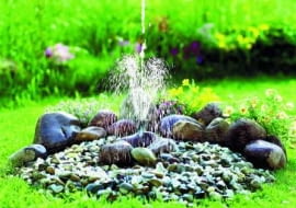 Prostota i minimalizm. Ukryta w zakopanym w ziemi pojemniku z wodą pompka tłoczy ją do dyszy wystającej z małegho kopczyka z kamieni.