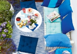 jA summery balcony seen from above with a laid table and aqua coloured cushions on white, outdoor furniture