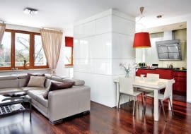 KUCHNIA. Za białymi frontami od strony pokoju kryją się schowki, m.in. barek. Dolne szafki kuchenne z lakierowanej na czerwono płyty MDF są przykryte blatem z konglomeratu kwarcowego - bardzo twardego, odpornego na ścieranie i działanie wysokiej temperatury.