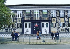 Dekoracja architektoniczna wykonana przez włoskiego artystę Opiemme na fasadzie jednej z łódzkich szkół. Mural reinterpretuje architekturę socrealizmu i czerpie z lokalnych tradycji