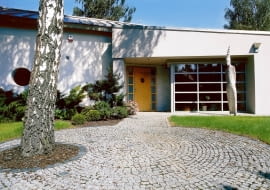 Wejścia do domu strzeże dwumetrowy totem. Drewniane drzwi - poszerzone i podkreślone wnęką ładnie kontrastują z aluminowymi elementami wykończenia budynku.