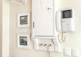 Dzięki naszemu pomysłowi przedpokój z zainstalowanymi na ścianie licznikami lub bezpiecznikami będzie wyglądał bardzo stylowo. Pokazana szafka jest łatwa do zrobienia i - co ważne - niedroga. <BR />Skrzynkę z licznikami lub bezpiecznikami najprościej jest ukryć w szafie ubraniowej - będą tam niewidoczne, a zarazem dostępne w razie potrzeby. Często jednak umiejscowienie tych niezbędnych, lecz nieatrakcyjnych urządzeń jest tak niefortunne, że nie ma mowy o jakiejkolwiek funkcjonalnej skrytce. Tak było w tym przypadku, stąd decyzja o zrobieniu ozdobnej miniszafeczki zharmonizowanej z wystrojem całego przedpokoju. Świetnym rozwiązaniem było umieszczenie obok szafki małych czarno-białych fotografii oprawionych w białe ramki - stanowią przeciwwagę wiszącego po prawej stronie domofonu.