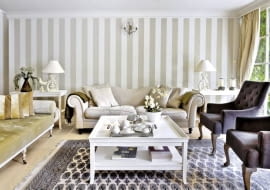 Ścianę pomalowano w szerokie szaro-beżowe pasy (podobny kolor mają obicia niektórych tapicerowanych mebli). Po obu stronach kanapy stoją stoliki pomocnicze; na nich wyeksponowano dekoracyjne przedmioty.