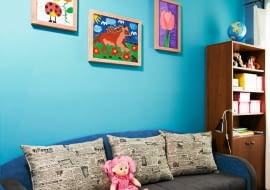 METAMORFOZY POKOJU DZIECKA. Starą sofę zastąpiono nową, większą. Mebel w zgaszonym odcieniu niebieskiego i chłodnej szarości ożywiły poduchy w modny gazetowy wzór. Tkaniny zostały wybrane z próbnika przez Maję i rodziców. Łóżko wygląda więc tak, jak chciała dziewczynka. Na jasnoturkusowej ścianie - wystawa prac Mai.