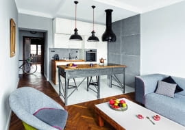 ANEKS KUCHENNY został optycznie wydzielony z przestrzeni dziennej innym kolorem podłogi. To taka sama dębowa klepka jak w pozostałej części pomieszczenia, tyle że pomalowana odporną na ścieranie farbą olejną. Nietypowa wyspa powstała ze stołu warsztatowego. Fragmenty ścian są pokryte betonowymi płytami. Zaimpregnowano je specjalnym preparatem, dzięki czemu nie chłoną plam.