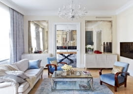 Pod symetrycznymi taflami postarzanych luster (Renes) stoją komody projektu Marii Kowalewskiej pokryte płatkami srebra. Jedna pełni funkcję barku, druga kryje sprzęt audio wideo. Kanapy (MTI Furninova), szklany stolik Cruise (BBHome). W głębi widoczna kuchnia i jadalnia.