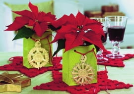 Ze złotym medalionem<br> Doniczki z poinsecją wstawiamy do papierowych torebek na prezenty. Do sznureczków przyczepiamy choinkowe zawieszki.