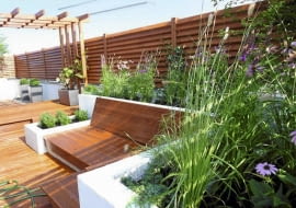 Rośliny balkonowe. Użycie drewna w ciepłym kolorze sprawia, że taras sprawia przytulne wrażenie. Będzie tu jeszcze ładniej, gdy pergolę oplecie winorośl