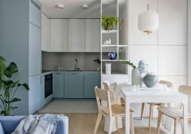 Otwarta, biało-niebieska kuchnia spójnie łączy się poprzez kolory i proste formy z aranżacją części dziennej. Piaskowy gres Marazzi na podłodze nawiązuje barwą do drewnianych akcentów w projekcie.