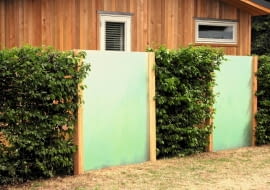 Ogrodzenie ze stalowej siatki (skrytej pod gałązkami formowanych krzewów) i tafli z tworzywa sztucznego, imitujących mleczne szkło.