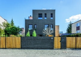 Pierwotnie na parceli stał niewielki budynek, który łączył się ścianą z sąsiednim. To, co zwykle uznawane jest za niedogodne (mało kto lubi bliźniaki), zostało w projekcie nowo powstałego domu obrócone na korzyść inwestorów - architekci wykorzystali każdy metr powierzchni działki