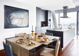 Obraz Doroty Buczkowskiej nad stołem w jadalni akcentuje szarości dominujące w tej części apartamentu. Na stole (Alivar): miseczki (Scandinavian Living), sztućce, obrus, i świeczniki (NAP). Wazon na kuchennej wyspie (Scandinavian Living). Meble w kuchni (Alno), sprzęt AGD (Miele).