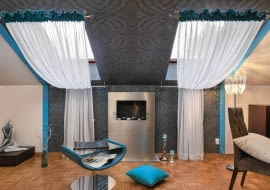 <B>Właścicielka mieszkania nie chciała zasłaniać okien dachowych typowymi roletami - marzyły jej się długie firany, które dodają wnętrzu lekkości i elegancji. Ale jak je zawiesić w takich oknach? Jest na to sposób.</B> <BR />Okienna aranżacja jest nie tylko efektowną ozdobą wnętrza - za firanami ukryto niezbyt estetyczne grzejniki. Sute marszczenie sprawia, że są one zupełnie niewidoczne.