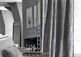 Zasłonę oraz poduszkę wykonano z tkaniny Eos. Bogaty barokowy wzór jest tylko o ton jaśniejszy od tła, dlatego wydaje się bardzo subtelny. Tak zaprojektowany materiał, mimo historycznego pochodzenia,świetnie sprawdzi się we wnętrzach współczesnych. Dostępny w pięciu wersjach kolorystycznych, Houles.