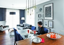 SPORY STÓŁ (ze sklepu Take me Home) z tapicerowanymi krzesłami (domartstyl.eu) przystawiono do wyspy. Ewa i Marek bardzo sobie chwalą to rozwiązanie, bo przygotowując posiłek dla gości, nie czują się wyłączeni z życia towarzyskiego. Ozdobą tej części pomieszczenia jest galeria grafik, zdjęć i plakatów oprawionych w białe i czarne ramki. Nad stołem - siedem lamp-żarówek (bylight.pl).