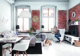 Duże okna szkoda było ukrywać za zasłonami, gospodarze wybrali więc żaluzje, które dobrze chroniąc przed słońcem, nie przesłaniają urody okien. Kanapa i fotel (ulubione miejsce Kasi i kotów) są z IKEA. Szafka pod telewizorem została 'stuningowana' - gospodyni pomalowała ją na biało i przykręciła nóżki z targu staroci. Pojemnik na koce (pod oknem) to znaleziony w piwnicy stary metalowy kosz na butlę z winem.