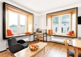 Okna są oprawione w monumentalne ramy - jak obrazy w muzeach. Wnęki okienne wyłożono płytą meblową fornirowaną naturalnym dębem, a otaczające je zewnętrzne profile pomalowano grafitową farbą i półmatowym lakierem. W kąciku do pracy stoi nowoczesny sekretarzyk Loft (ze sklepu Inne Meble). Jak większość wyposażenia, jest wykonany z drewna dębowego. Ciemne stalowe profile nawiązują do obudowy okien. Na ścianie - dyskretny reflektorek z kolekcji Atelier.