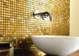 Łazienkę, zwłaszcza w miejscach narażonych na zachlapanie, najczęściej wykańczamy praktycznymi, trwałymi płytkami ceramicznymi - idealnymi do pomieszczeń, w których panuje wilgoć. Można je jednak zastąpić innymi materiałami. Jakimi? Mamy kilka sugestii. <BR /> ŁAZIENKA. Tapeta i szkło. Iście po królewsku: mieniąca się w świetle szklana mozaika w kolo-rze złota doskonale pasuje do dekoracyjnej ramy lustra.