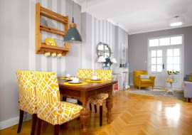 Stylizowany dębowy stół o pięknych toczonych nogach Alina wypatrzyła w sklepie z używanymi meblami (tam znalazła też szafę do sypialni). Do stołu dobrała krzesła z IKEA, którym sprawiła nowe pokrowce w swoim ulubionym żółtym kolorze. Meble stoją na tle tapety w szerokie pasy (firmy Rasch). W głębi widać salonik, a w nim imitację kominka zrobioną przez stolarza. Przed kominkiem 'wygrzewa' się porcelanowy chart.