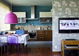 KOLOROWA I WESOŁA. Fantazyjne abażury: z pomalowanej na różowo wikliny oraz z koronki zastąpiły wiszące tu wcześniej lampy o prostych formach. Z kolorystyką wnętrza harmonizuje tapeta w kwiatowy wzór, którą pokryto ścianę przesłaniającą aneks kuchenny.