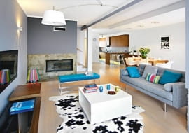 Dom Justyny i Krzysztofa miał być jasny i przestronny. Nowoczesny, ale w żadnym razie nie chłodny. Praktyczny, ale nieprzeładowany przedmiotami. a do tego utrzymany w delikatnych, uspokajających barwach, które łatwo urozmaicić kolorowymi dodatkami. <BR /> WNĘTRZA. Ściany w salonie pomalowano na dwa odcienie szarości. Betonowy fragment wokół kominka pokryto żywicą, stąd ciekawy wzór i kolor. Kąt wypoczynkowy oświetla lampa wisząca, przypominająca nieco przeskalowaną lampę biurkową, oraz zabawna lampka-łowiczanka, autorstwa polskiej projektantki Katarzyny Herman-Janiec.